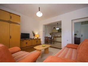 A living room with orange sofas, a wooden cabinet, a TV, and a dining area with chairs and a table.