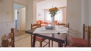 A dining area with a table set for four, surrounded by wooden chairs. A vase with flowers is placed on the table, and there is a window with curtains in the background. - Apartments Andrea (Crikvenica)