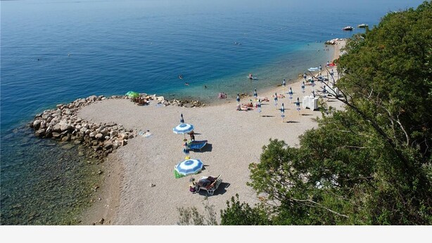 A beach with clear water, a rocky shoreline, and several umbrellas. - Apartments Andrea (Crikvenica)