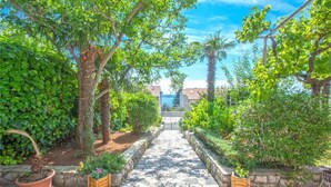 A stone pathway leading to a gate, flanked by lush greenery and potted plants. - Apartments Andrea (Crikvenica)
