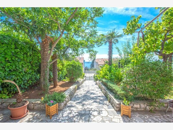 A stone pathway leading to a gate, flanked by lush greenery and potted plants.