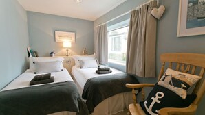 Ein Zimmer mit zwei Betten, einem Holzstuhl, einer Lampe und einem Fenster mit Vorhängen.