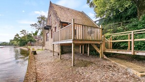 A rustic wooden building with a sloped roof, a wooden deck, and a stone foundation near a body of water. - Creinch Lodge-Sleeps 2 - sleeps 2 guests  in 1 bedroom (Alexandria)