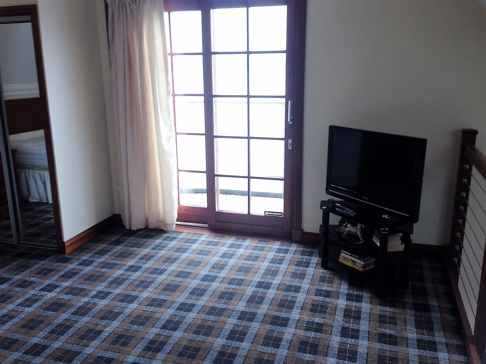 Habitación de hotel con suelo a cuadros, un televisor sobre un mueble y una puerta con vistas al exterior.