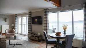 Un salon moderne doté d’une grande fenêtre, d’un téléviseur à écran plat et d’un coin repas avec une table et des chaises.