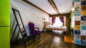A room with a wooden floor, a bed with a wooden headboard, a chair, a mirror, and a colorful tiled wall.