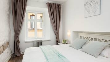 A bedroom with a bed, curtains, a radiator, a window, and a wall-mounted light fixture.