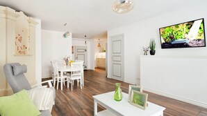 A modern living room with a dining area, wooden flooring, a white sofa, a coffee table, and a TV mounted on the wall. - Blacksmith Old Town Apartments (Tallinn)