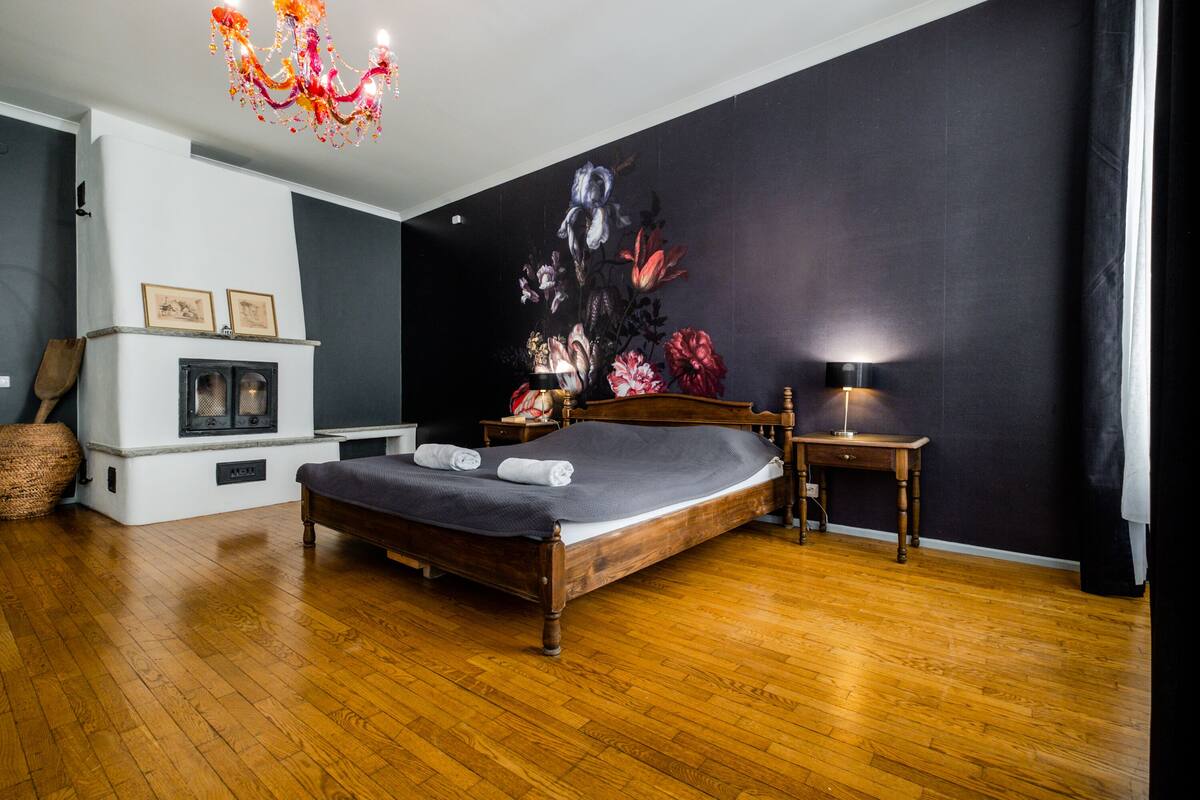 Ein Schlafzimmer mit einem hölzernen Bett, einem Nachttisch, einer Lampe, einem Kamin und einem großen floralen Wandbild.