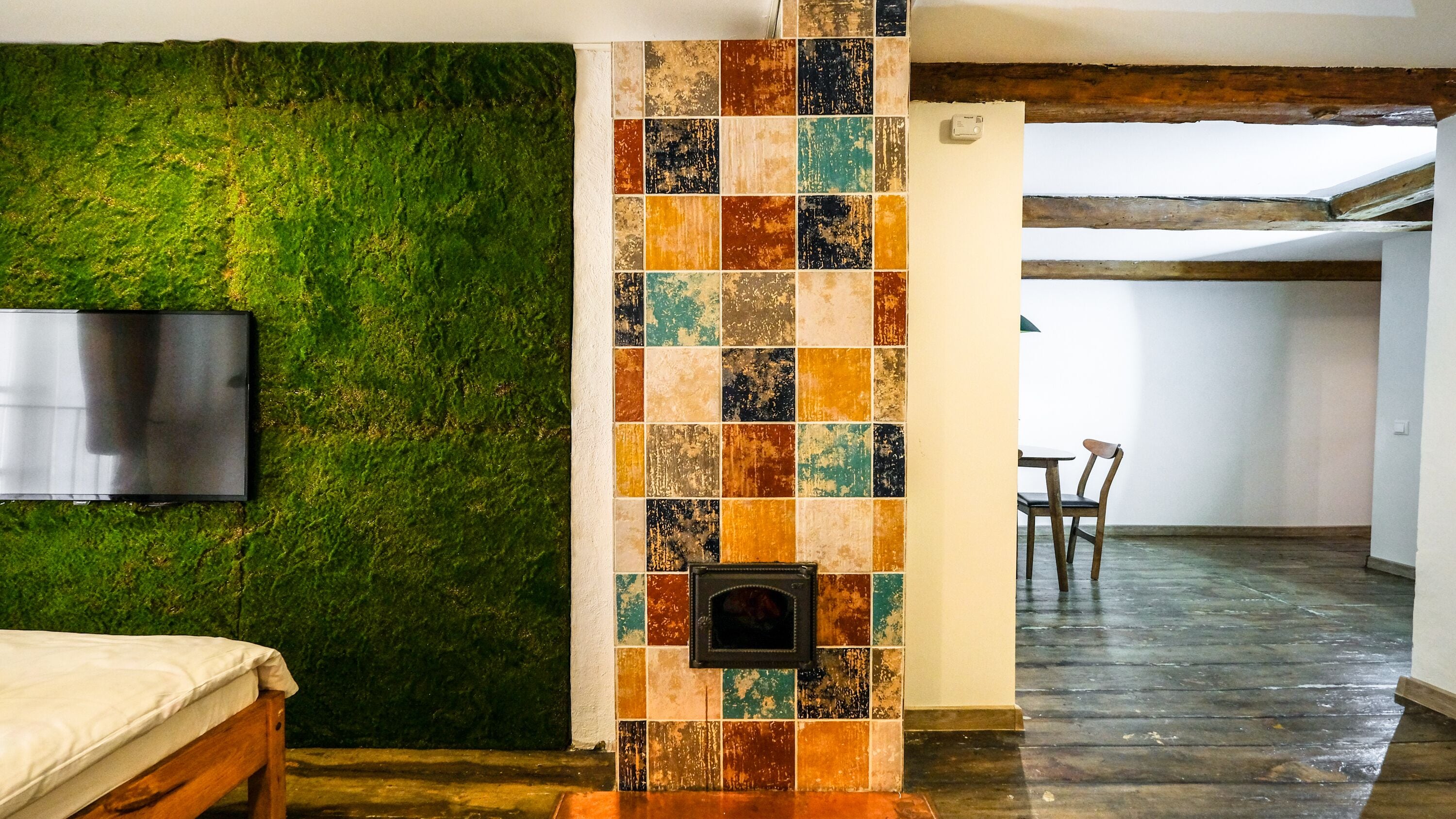 Una habitación con pared verde texturizada, una columna con azulejos, una cama, un televisor y un área de comedor con sillas.