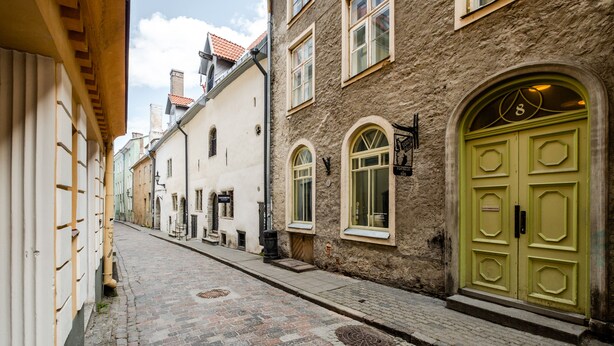 A narrow cobblestone street lined with historic buildings, featuring a prominent green door and a small window with a sign. - Blacksmith Old Town Apartments (Tallinn)