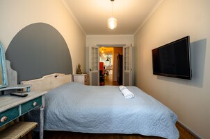 Een slaapkamer met een bed, een bureau, een stoel, een televisie en een boogvormige deuropening naar een andere kamer.