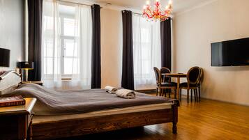 Ett hotellrum med en säng i trä, ett skrivbord med en stol, en tv och en kristallkrona.