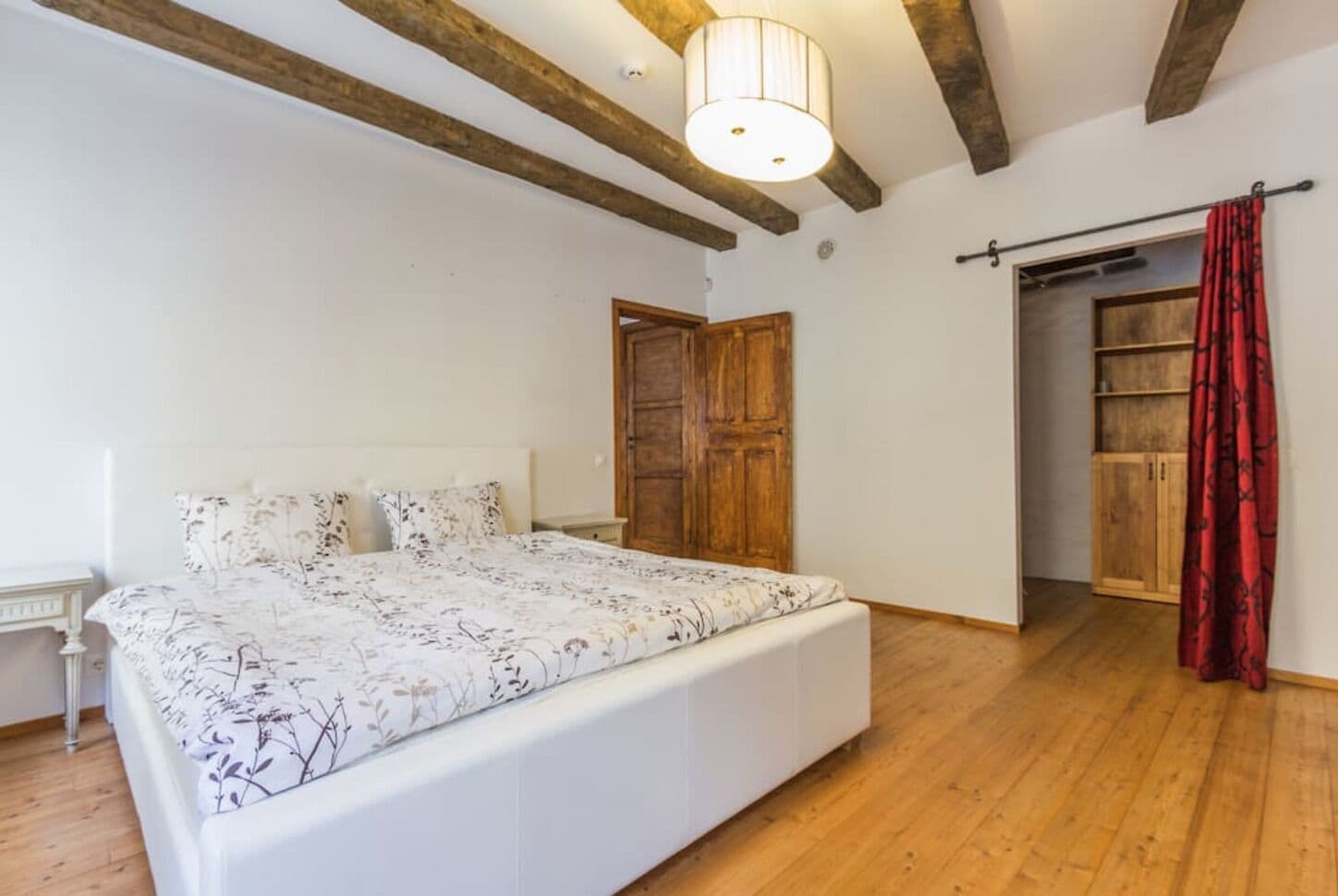 Camera da letto con un letto grande, travi in legno a soffitto, un armadio e una porta con tenda rossa.