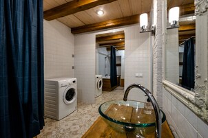 Een badkamer met een glazen wastafel, twee wasmachines en een houten wastafelmeubel.