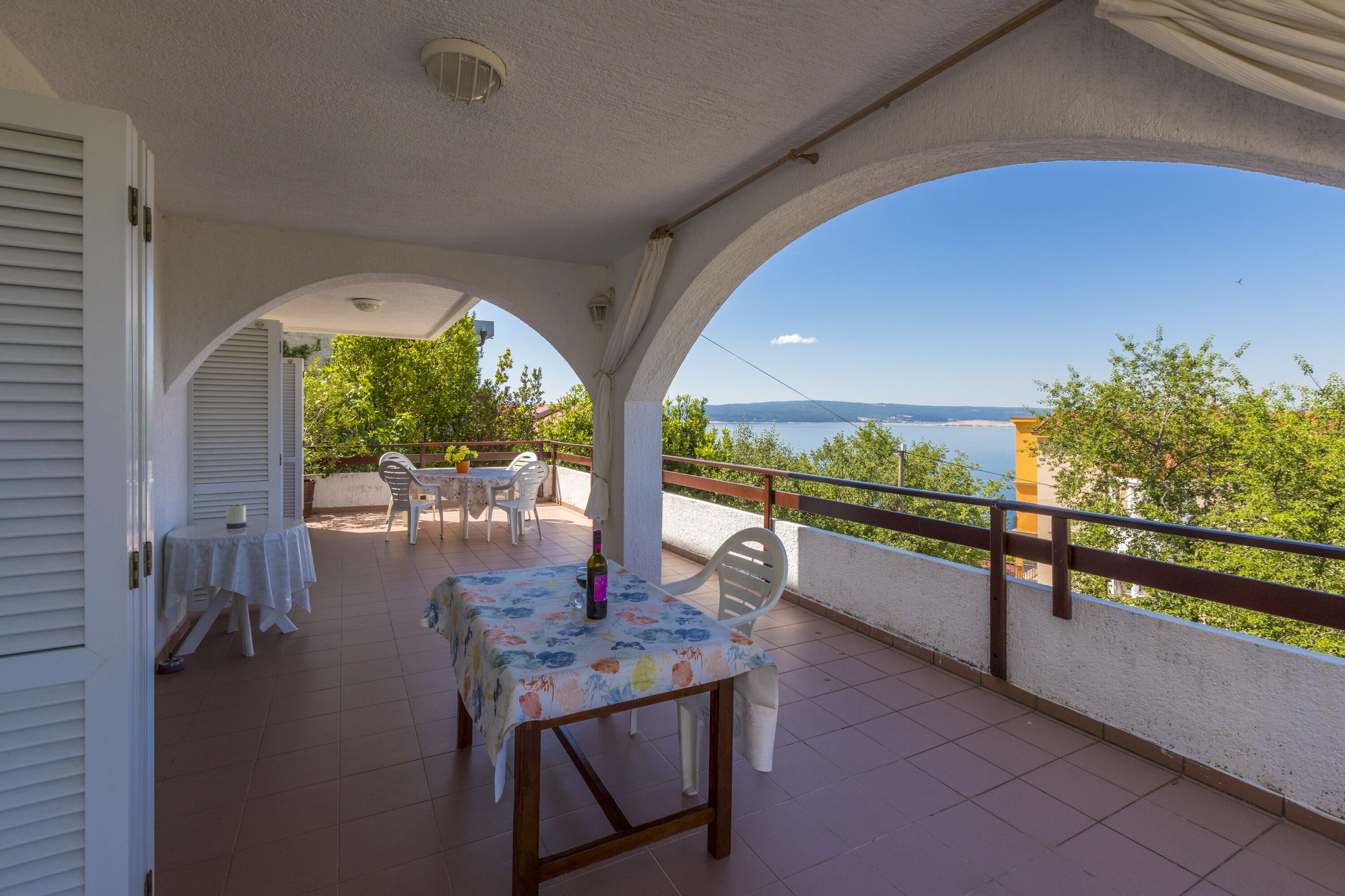A covered outdoor patio with a table and chairs, a view of the sea, and a railing.