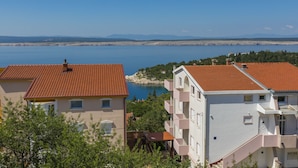 A coastal building with a red-tiled roof, adjacent to a body of water and mountains in the background. - Apartments Gordana (Crikvenica)