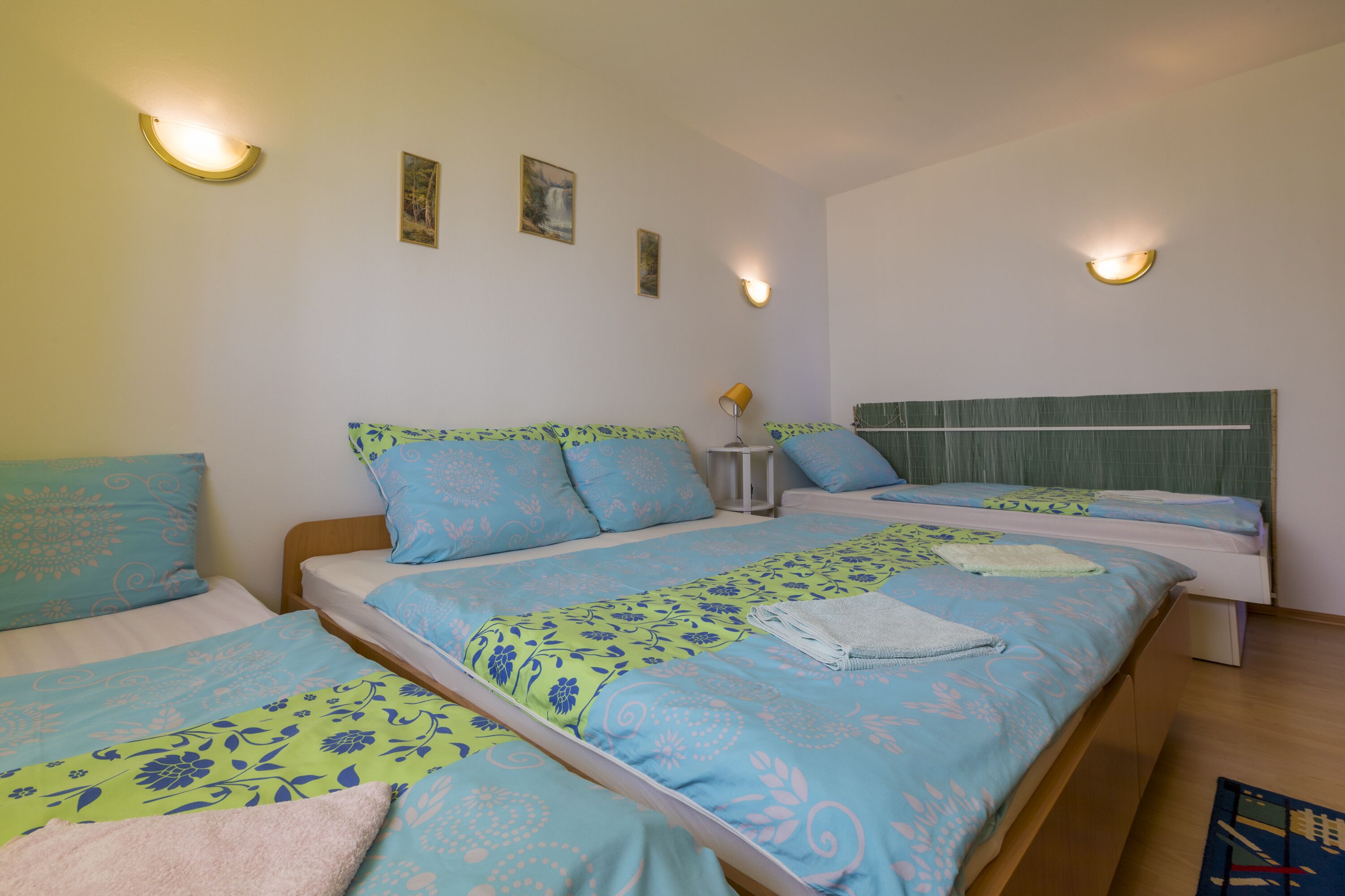 Une chambre avec deux lits, chacun agrémenté de draps à motifs floraux, une table de chevet avec une lampe et des appliques murales.