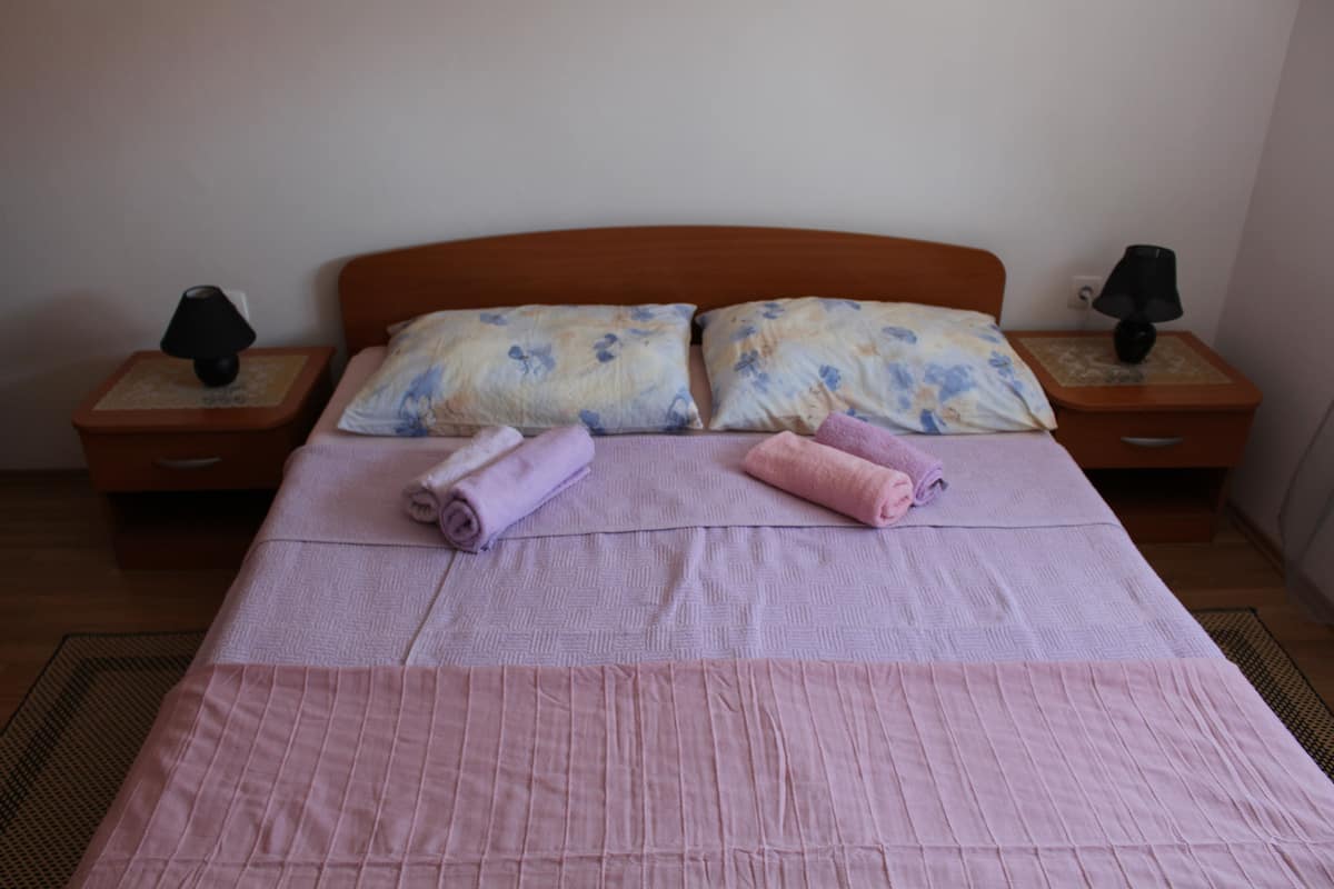 Un lit bien fait, avec du linge de lit rose et deux oreillers, deux tables de chevet avec des lampes et une tête de lit en bois.
