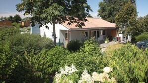 Ein Bungalow mit rotem Ziegeldach, umgeben von üppiger Vegetation und blauem Himmel.