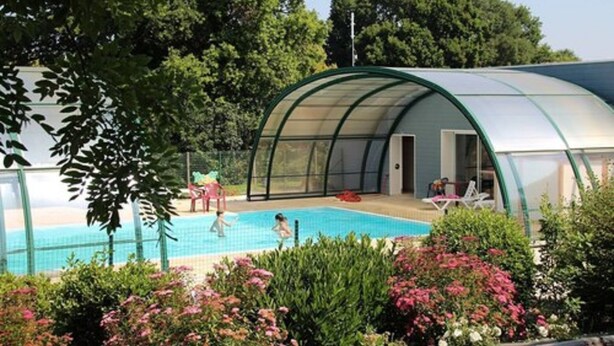 Ein überdachter Pool mit gewölbter Dachkonstruktion, umgeben von üppiger Vegetation und blühenden Pflanzen.