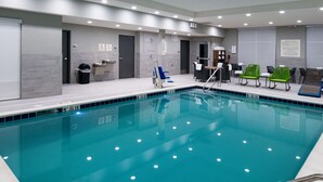 A swimming pool with a tiled edge, a changing room, and a seating area with chairs.