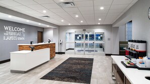 A reception area with a wooden reception desk, a welcome sign, a glass door entrance, and a small kitchenette with a coffee machine.