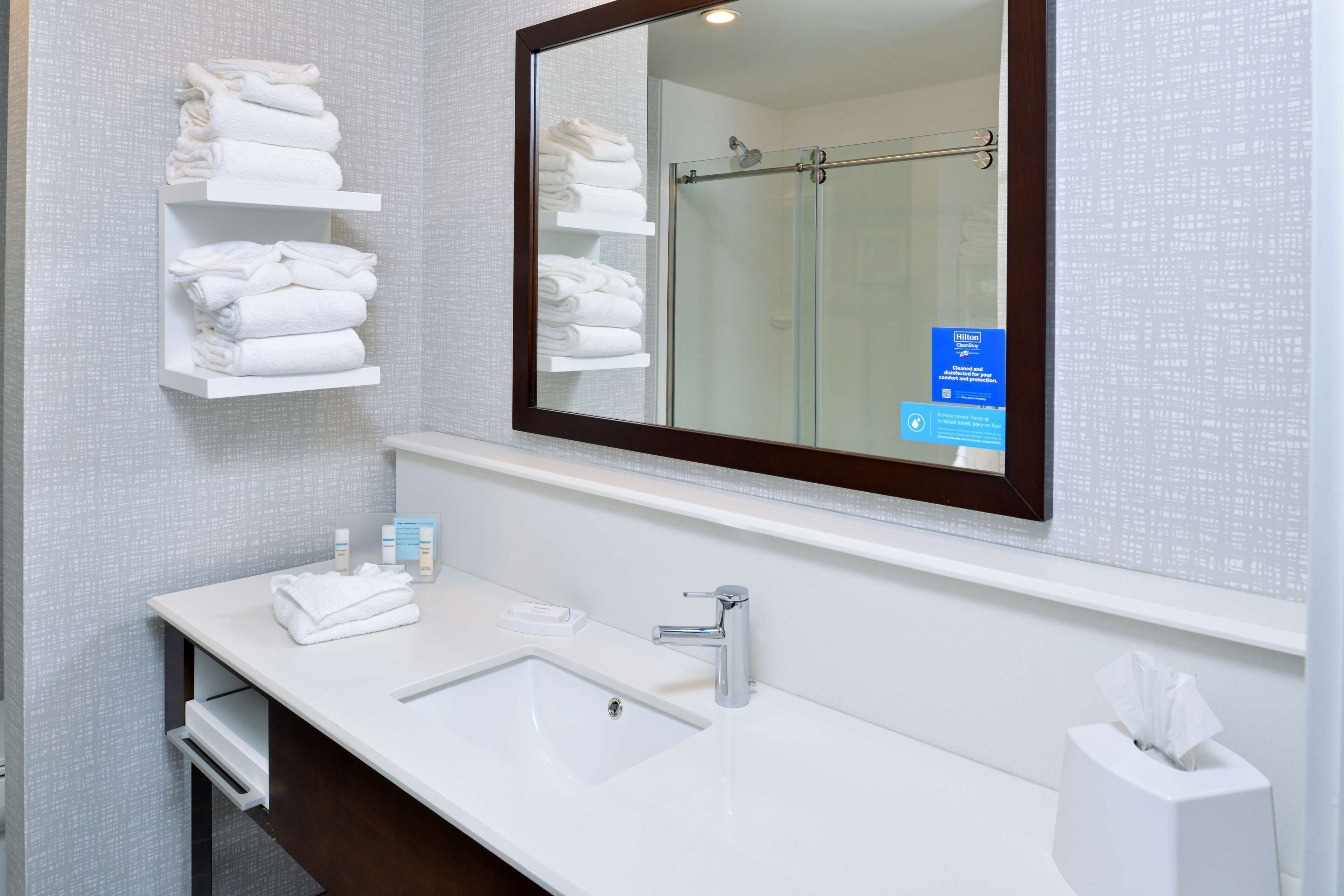 Un baño con lavamanos blanco, un espejo y estantes con toallas dobladas.