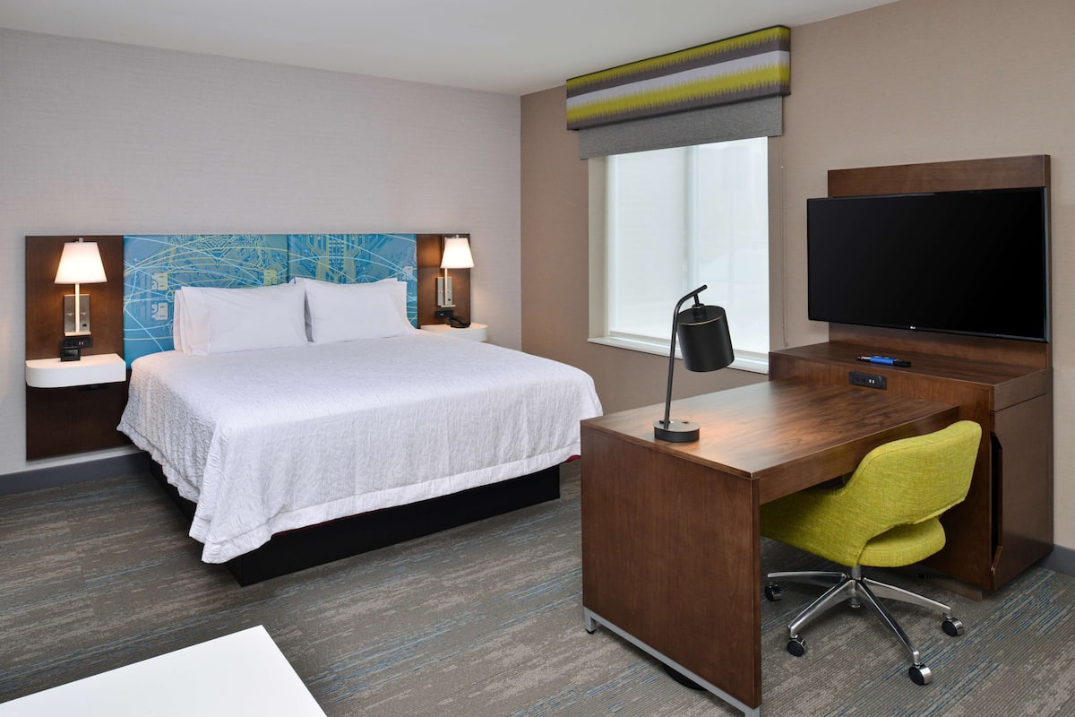 A hotel room with a bed, desk, TV, and two bedside lamps.