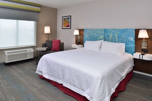 A hotel room with a large bed, two bedside tables with lamps, a window with a view, a wall-mounted air conditioner, and a red accent wall.