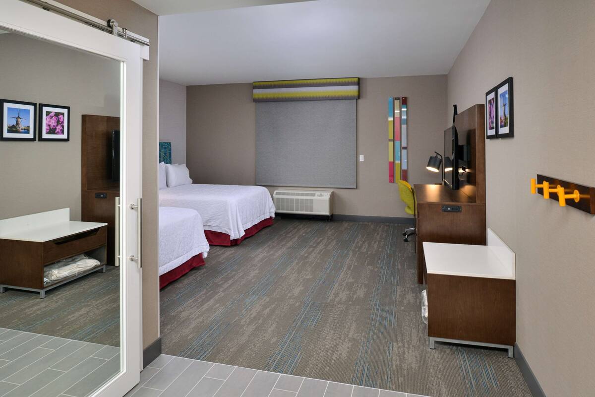 A hotel room with two beds, a bathroom, a large window with a view, and a flat-screen TV.