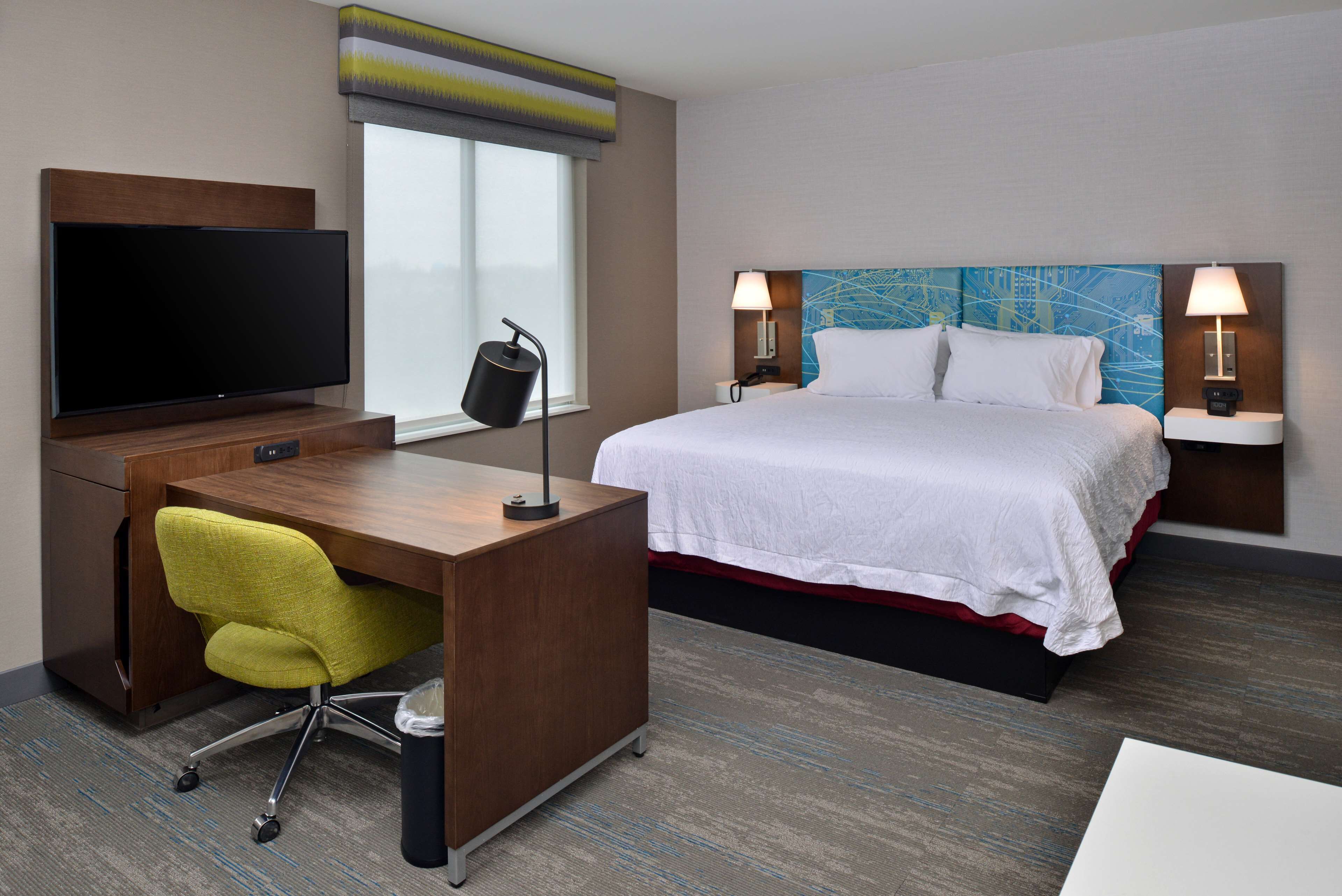 Een hotelkamer met een bed, een bureau met een televisie, een stoel en twee bedlampen.