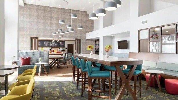 A modern interior with a long communal table, teal chairs, and a bar area.