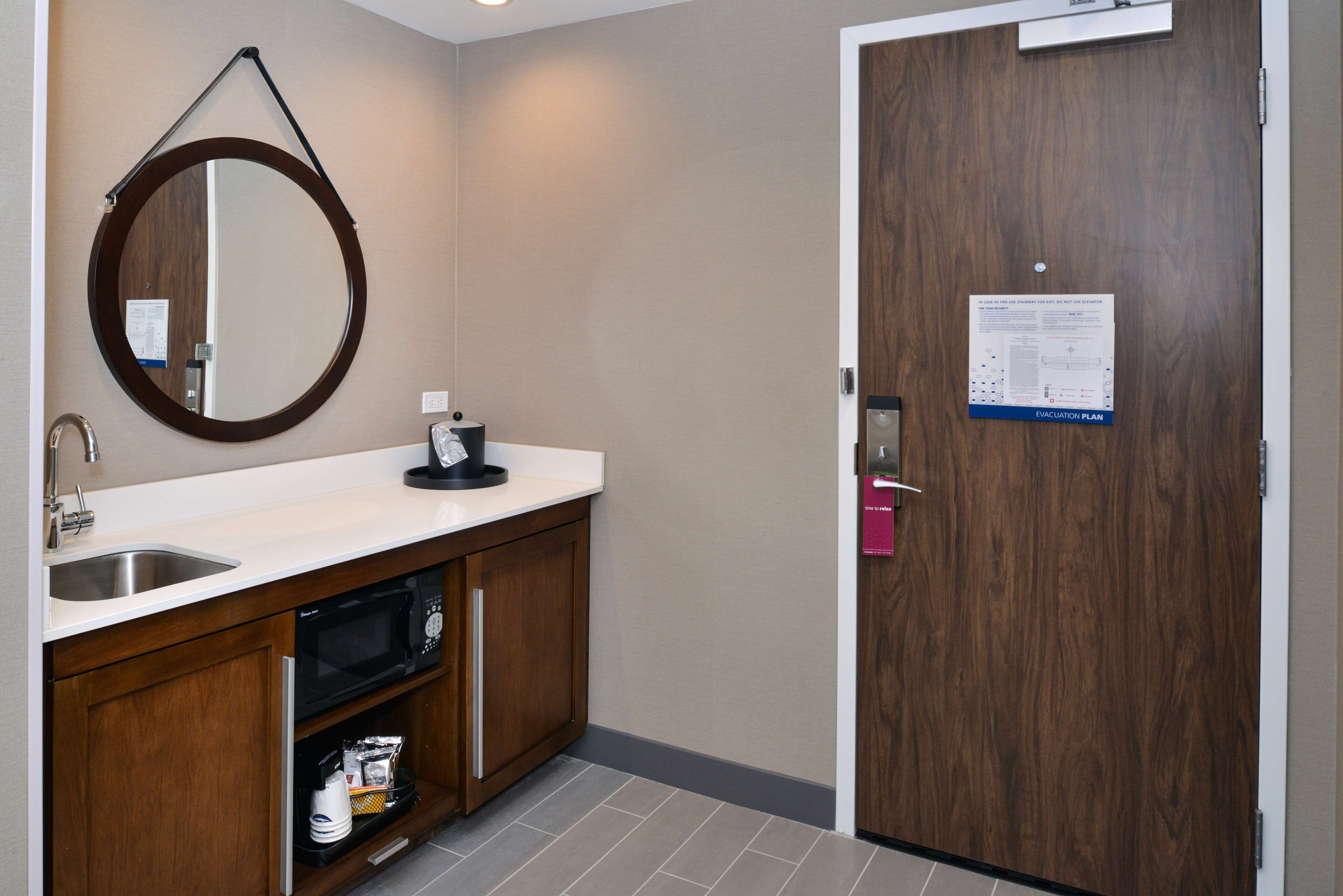 A bathroom with a sink, mirror, and a wooden door with a posted evacuation plan.