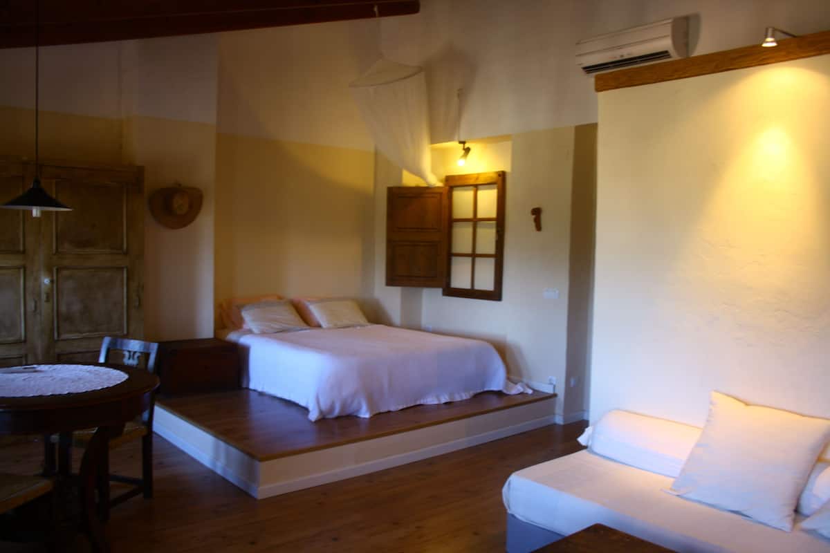 Un dormitorio con cama, un pequeño sofá, una mesa de madera y una silla.