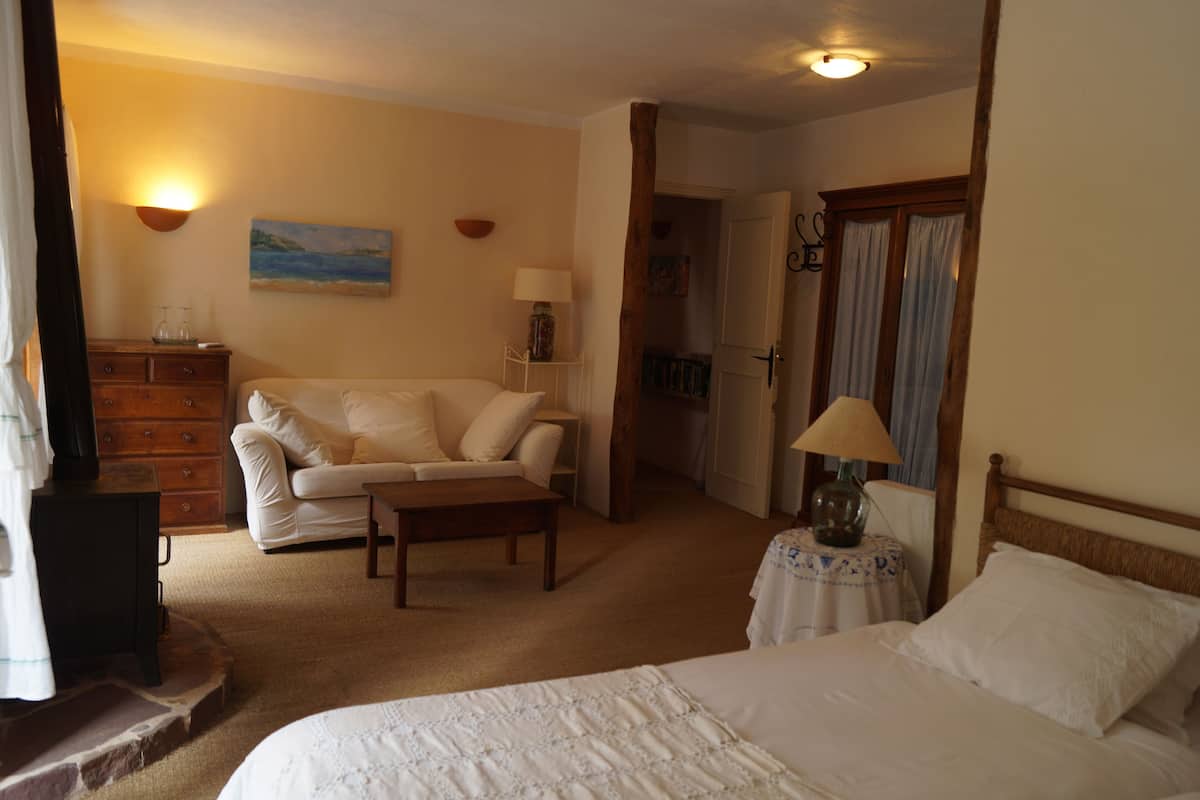 Una habitación de hotel acogedora con una cama, un sofá, una mesita, una lámpara, un aparador y un cuadro en la pared.