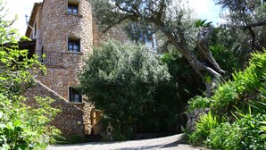 A stone building with a curved tower, surrounded by lush greenery and trees. - Sa Plana Petit Hotel (Estellencs)