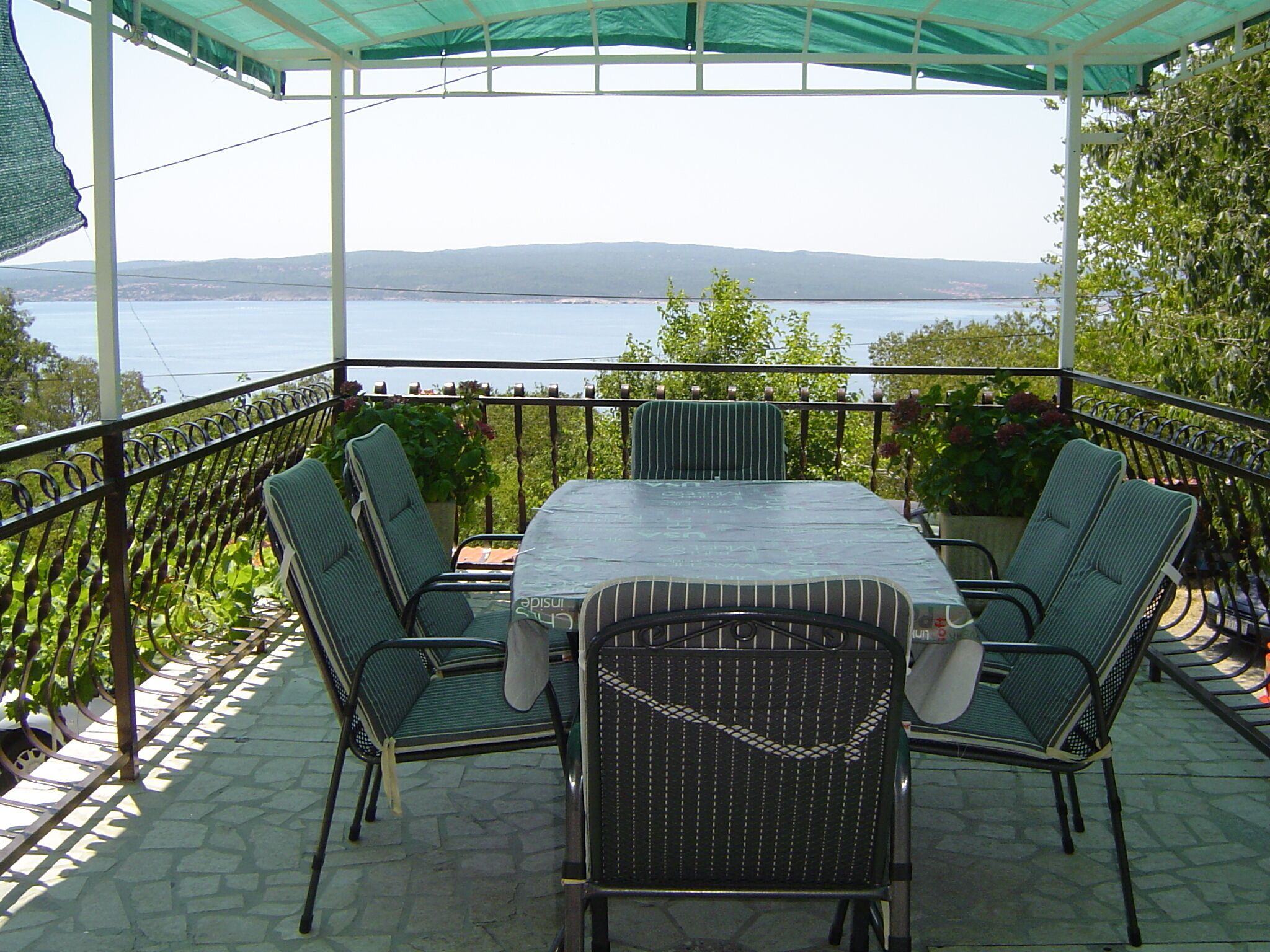 An outdoor patio with a table and four chairs, overlooking a body of water and hills.