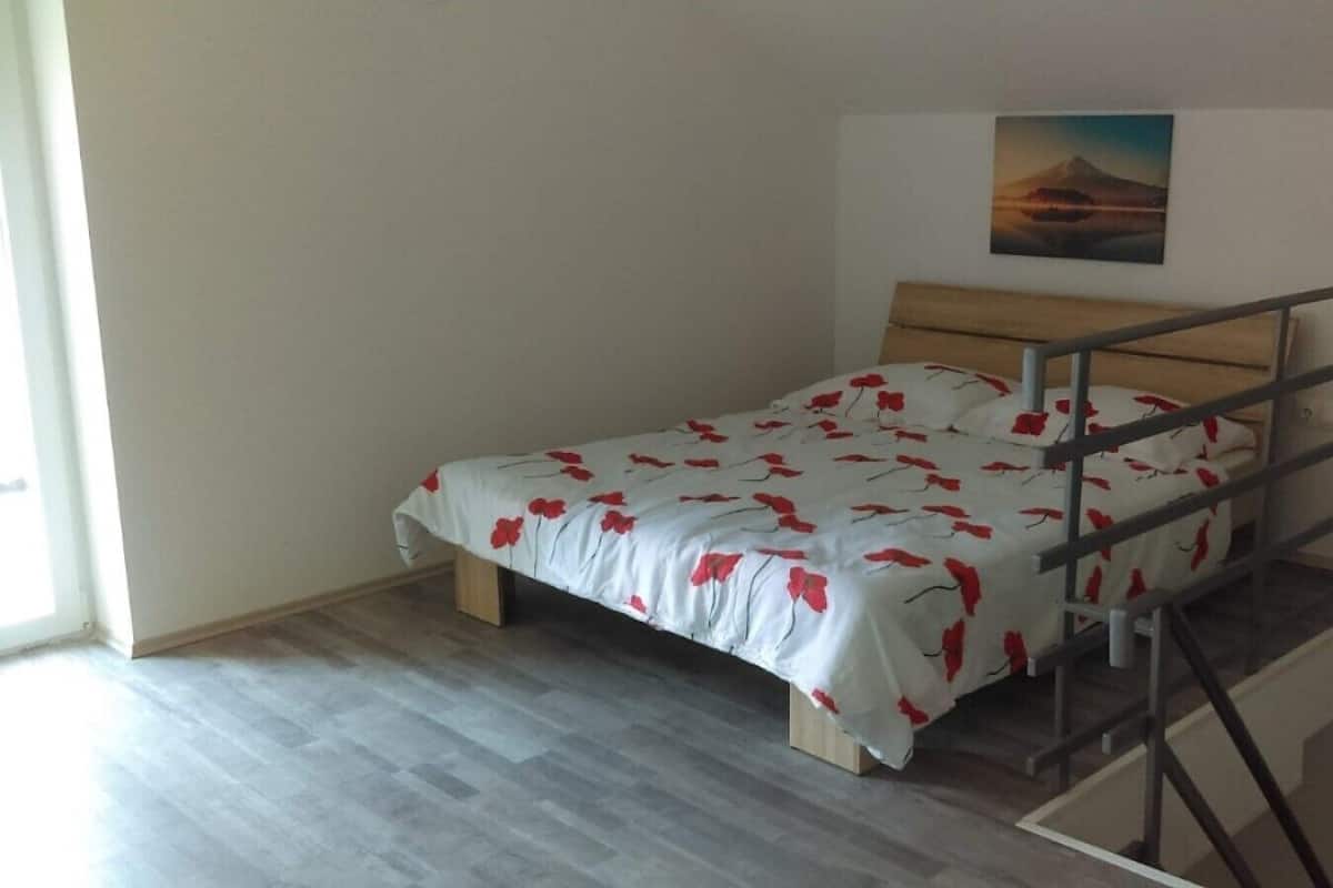 A single bed with a metal frame and a wooden headboard, positioned against a plain wall with a framed picture above it.