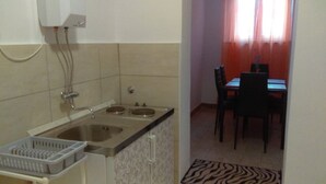 A small kitchen with a sink, two burners, and a countertop. There is a dining area with a table and chairs visible through an open door. - Apartments Iva (Crikvenica)