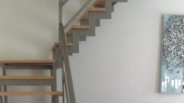 A staircase with wooden steps and metal railings, leading to a dark-colored sofa and a wall-mounted abstract art piece. - Apartments Iva (Crikvenica)