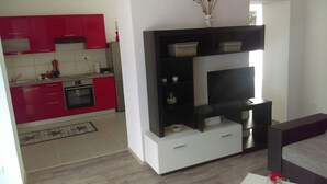 A modern living room with a flat-screen TV, a black entertainment unit, and a red kitchen in the background. - Apartments Iva (Crikvenica)
