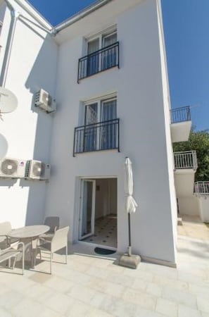 A multi-story building with balconies, a covered outdoor seating area, and a door leading to an interior space. - Apartments Silly (Crikvenica)