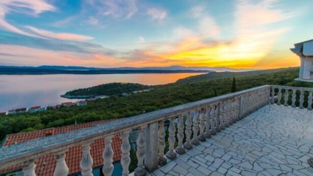 A balcony with a stone floor and balustrade, overlooking a body of water and a distant island. - Apartments Silly (Crikvenica)
