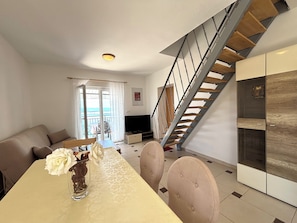 A modern living room with a dining table, sofa, and a staircase. - Apartments Silly (Crikvenica)
