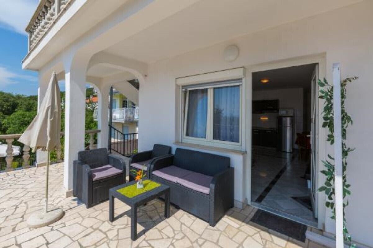 Zona relax esterna coperta con due divani e un tavolo, una porta in vetro che dà su una cucina e un pavimento in pietra.
