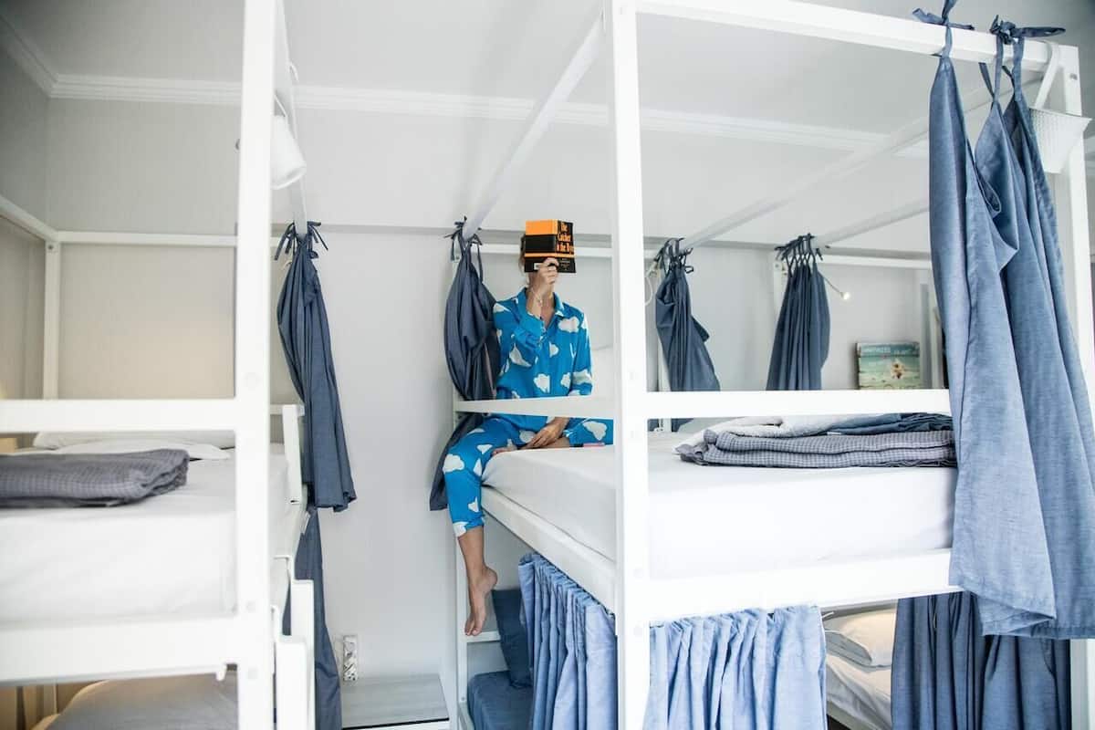 A bunk bed room with a person sitting on the top bunk.
