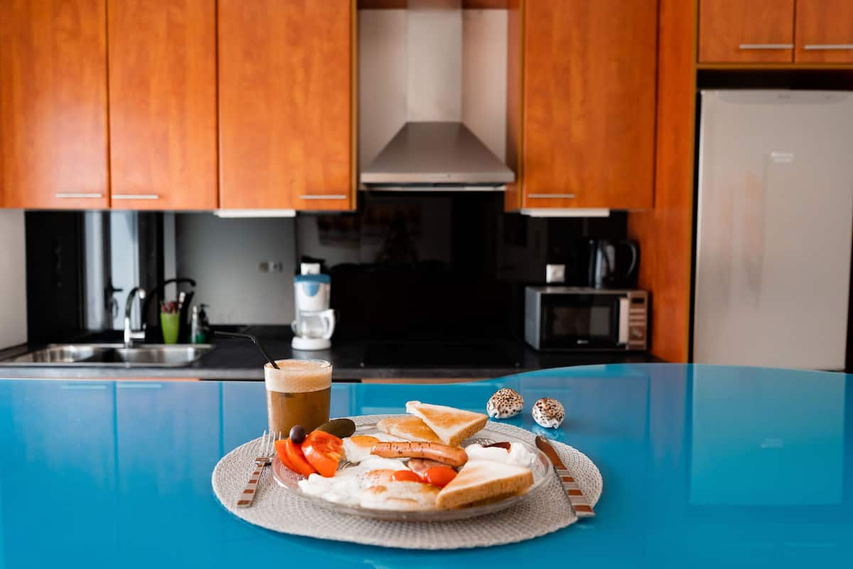 A breakfast tray with toast, eggs, sausages, and tomatoes on a blue table in a kitchen with wooden cabinets and a microwave.