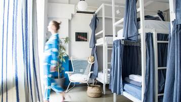 A room with bunk beds, a white chair, a potted plant, and a wall-mounted air conditioner.