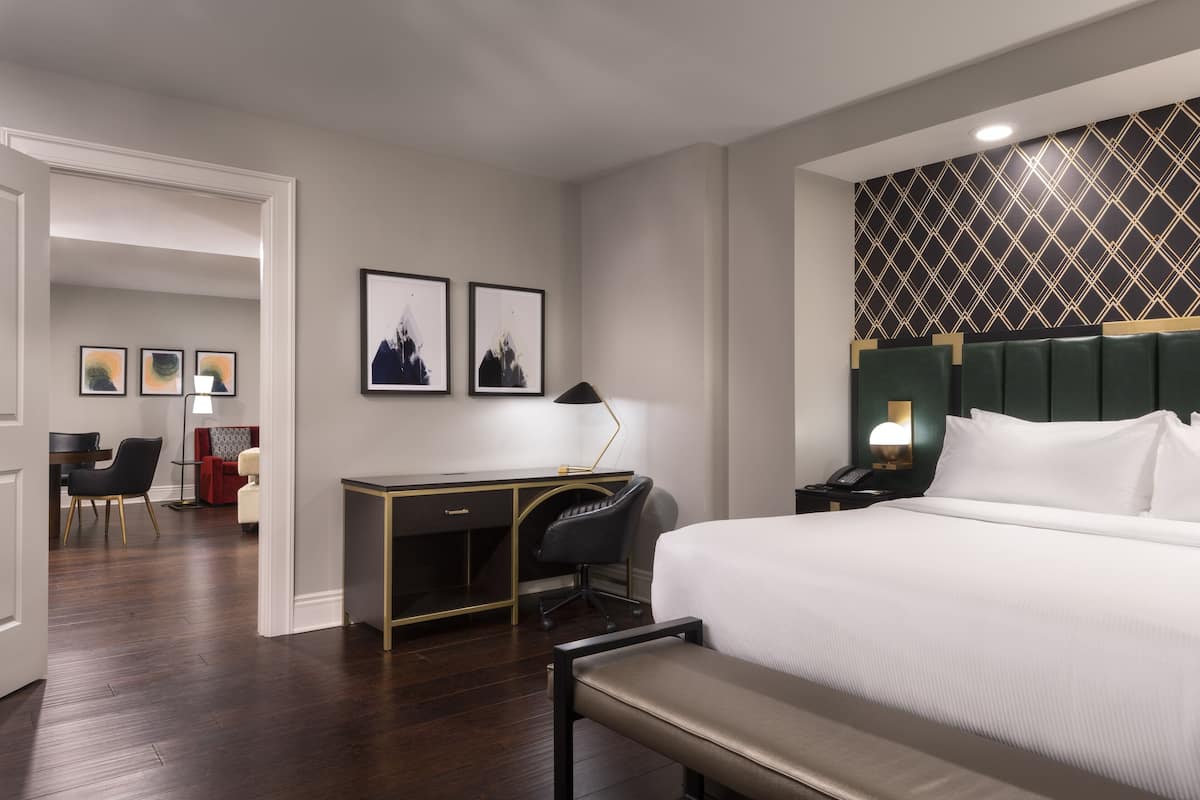A hotel room with a large bed, a desk with a chair, a desk lamp, and framed pictures on the wall.